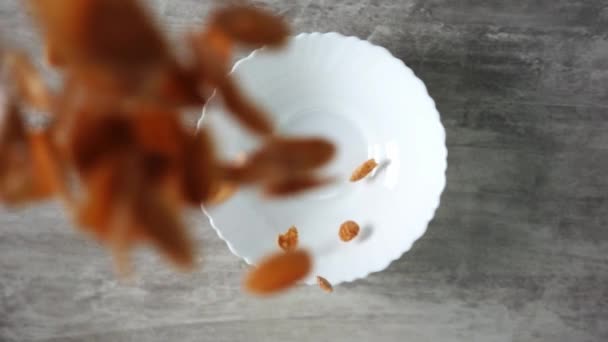 Les flocons de maïs tombent dans un plat blanc debout sur une table en bois au ralenti filmé d'en haut — Video