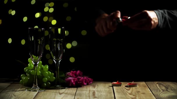 Mans mãos queimando velas e colocando em mesa de madeira ao lado de dois copos de vinho e rosas — Vídeo de Stock