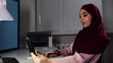 Başörtülü Müslüman iş kadını akıllı telefonuyla video konuşmalarıyla konuşur ve notlar alır.