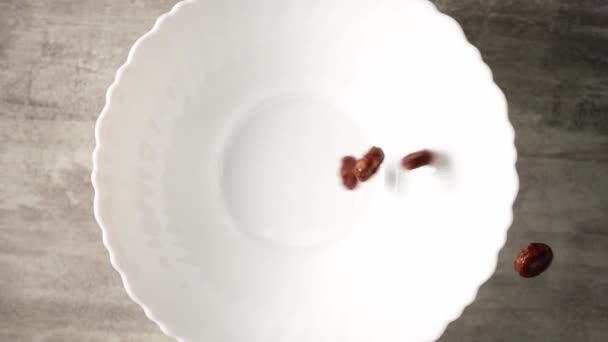 Шоколадні кукурудзяні пластівці у вигляді кілець вливаються повільно в білу тарілку — стокове відео