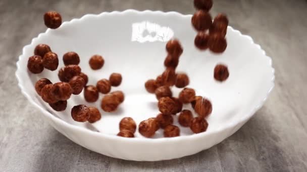 Rzucanie płatków czekoladowych w postaci kulek do białego naczynia stojącego na stole w slowmo — Wideo stockowe