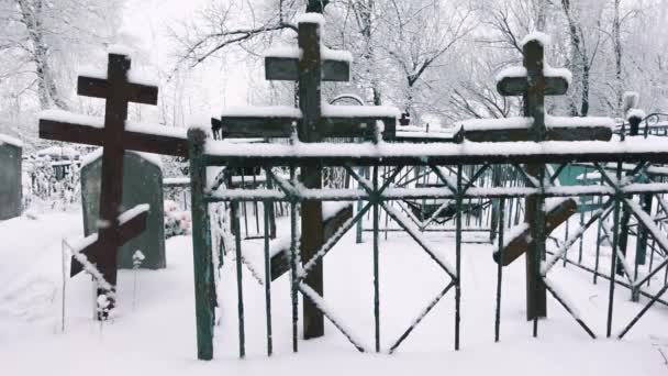 Uitzicht op de begraafplaats met de houten kruisen en hekken tussen vallende sneeuwvlokken in een slow motion — Stockvideo