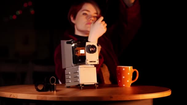 Portrait of woman who sit at the table where there is a slide projector and watch photo negatives — Stok Video