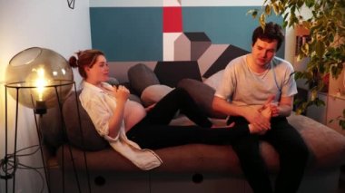 Hamile kadın kanepede uzanıyor ve erkek ayaklarına masaj yapıyor.