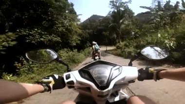 Palmiye ağaçları, ormanın içinden geçen scooter 'ın dikiz aynasına yansıyor.