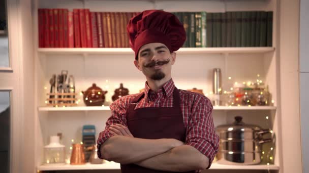 Portrait of smiling young cook wearing red toque with apron and standing with crossed arms — Stock Video