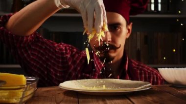 Kırmızı toka parçacıkları serpiştirilmiş bir şef yavaş yavaş enchilada pişirirken tortilla üzerine peynir rendeledi.