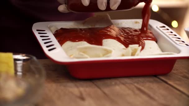 Macro uitzicht op chef-kok handen in handschoenen staande aan houten tafel en gieten enchilada door tomatensaus — Stockvideo