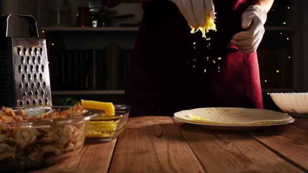 Cozinhe as mãos em luvas jogando queijo ralado na tortilla deitado na placa em uma mesa de madeira em slowmo — Vídeo de Stock