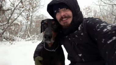 Köpeğiyle birlikte bir sahibi, kış ormanında, yavaş yavaş düşen karın arasında selfie çekiyor.