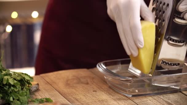 Close-up de mãos de chef que estão pegando um pedaço de queijo e começar a ralar em uma caçarola de vidro — Vídeo de Stock