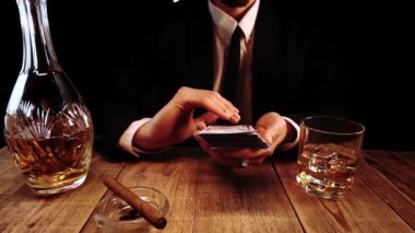 Yakından çekilen görüntülerde siyah kostümlü zengin bir adam barda oturuyor ve bir tomar banknot atıyor.