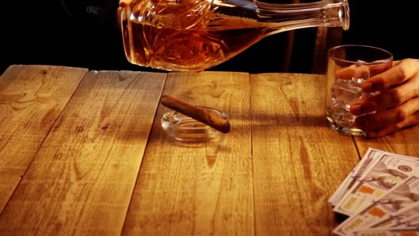 木製のテーブルに座っていて、ゆっくりとガラスの中にウイスキーを注ぐ人の手のクローズアップビュー — ストック動画
