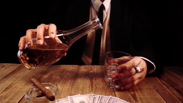 Een man in een elegant pak giet cognac uit een kan in glas in close-up in slow motion. — Stockvideo