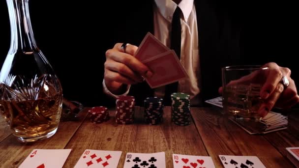 Άντρας με μαύρη στολή παίζει πόκερ κάθεται σε ένα ξύλινο τραπέζι και ρίχνει δύο άσους σε αργή κίνηση — Αρχείο Βίντεο