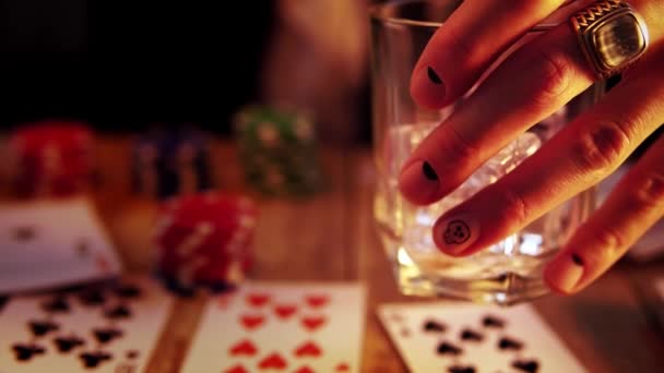 Χέρι του ανθρώπου με μανικιούρ κρατά ένα ποτήρι γεμάτο πάγο και ρίχνει ουίσκι σε αυτό κατά τη διάρκεια του παιχνιδιού πόκερ — Αρχείο Βίντεο
