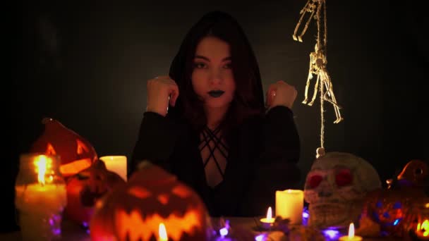 Mulher em um manto senta-se à mesa com decorações de Halloween no fundo preto — Vídeo de Stock