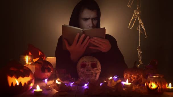 Portrait of man in the image of wizard reading voodoo book among candles and jack olanterns — Stock Video