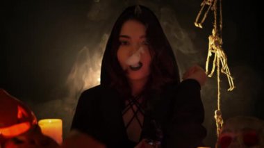 Siyah mantolu, gotik makyajlı güzel bir kadın elektronik sigara içiyor.