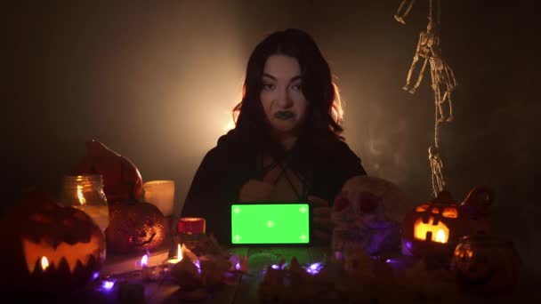 Heks beveelt een mobiele met chroma sleutel zitten tussen Halloween decoraties — Stockvideo