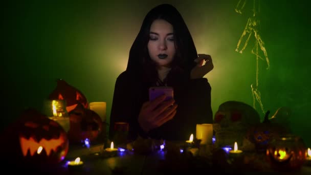 Жінка в готичному костюмі сидить і дивиться смартфон в її руках серед прикрас Хеллоуїна — стокове відео