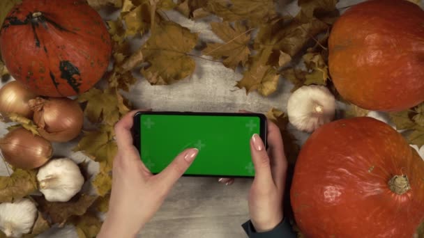 Mulher bate em um telefone greenscreen na orientação horizontal entre as decorações de outono — Vídeo de Stock