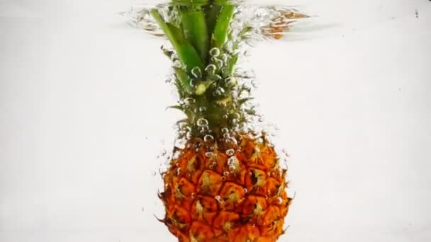 De ananas valt met veel belletjes in het water. Vruchten op geïsoleerde witte achtergrond. — Stockvideo