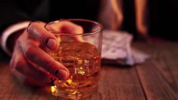 L'uomo si siede a un tavolo di legno rotolando vetro con whisky in mano e lancia due dadi in macro — Video Stock