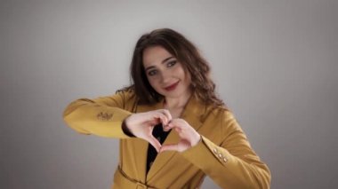 Kafkasyalı genç bir kadının portresi yavaş çekimde beyaz arka planda kalp şeklini elleriyle gösteriyor.