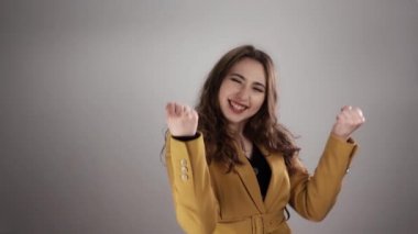 Yumruklarını beyaz arka planda yavaş çekimde sıkan mutlu ve memnun bir kadının portresi.