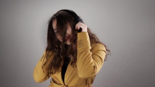 Retrato de una joven escuchando música con auriculares y bailando sobre fondo blanco en slow mo — Vídeos de Stock