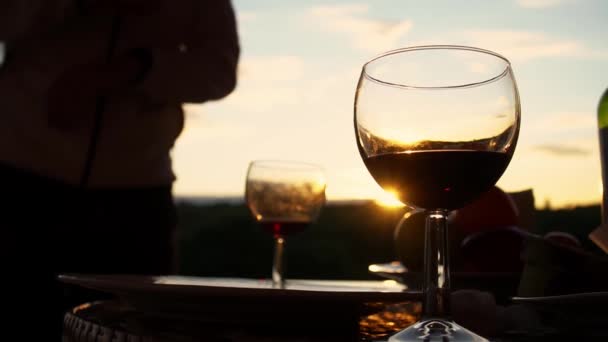 Vista de perto do copo de vinho em pé na mesa de piquenique no fundo do pôr-do-sol e homem tomando outro — Vídeo de Stock