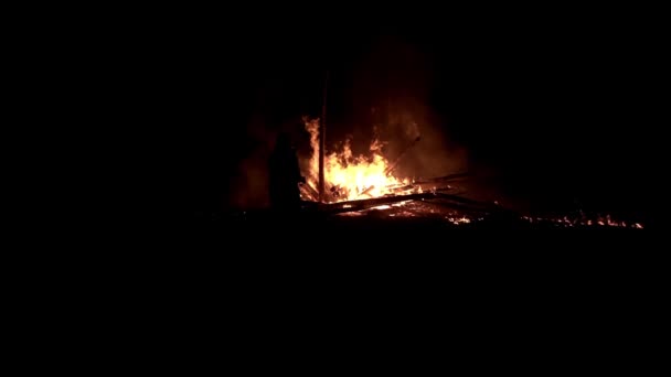 Een man staat en kijkt naar een afgebroken brandend kampvuur 's nachts in slow motion — Stockvideo