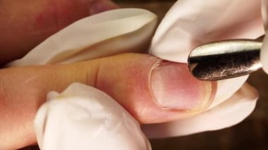 Macro of manicurist hands cleaning and removing cuticle by a metal pusher filmed from above