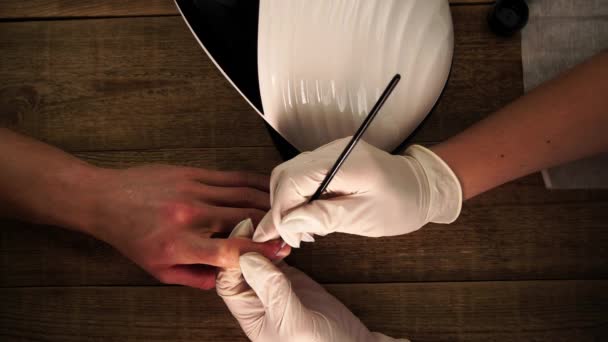 Tırnak ustası, yukarıdan çekilen güzellik prosedürü sırasında fırçayla erkek müşteriye resim tasarımı yapıyor. — Stok video