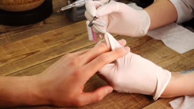 Koruyucu eldivenli bir manikürcü, metal iticisiyle tırnak etlerini temizleyip çıkarıyor.