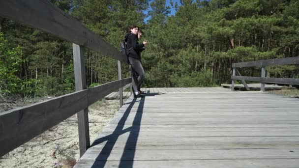 Γυναίκα και άνθρωπος στέκονται στην ξύλινη γέφυρα με το δάσος στο παρασκήνιο την ηλιόλουστη μέρα — Αρχείο Βίντεο