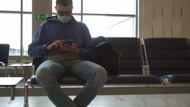 Homme portant un masque de protection se trouve dans le terminal de l'aéroport avec smartphone à la main et attend le départ — Video