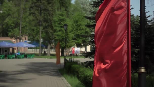 Saténově červená vlajka se vyvíjí v městském parku v létě ve zpomaleném filmu — Stock video