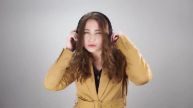 Kulaklıkla müzik dinleyen ve beyaz bir arka planda dans eden neşeli kadının portresi.