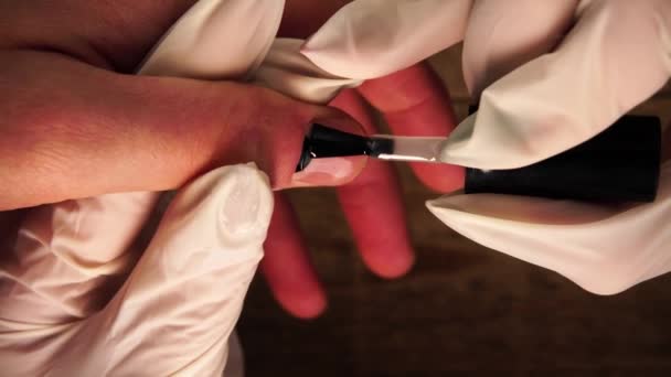 Maniküre in Schutzhandschuhen trägt transparentes Gel-Schellack auf Kundennägel mit Kunstdesign auf — Stockvideo