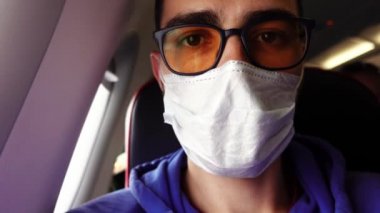 Tıbbi maskeli bir adamın Selfie 'si. Uçakta oturmuş, uçuşu bekliyor.