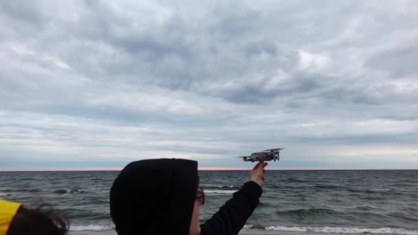 Man and woman are standing next to the ocean and piloting the drone to the sky in a slow motion — Stock Video