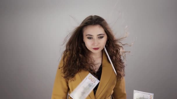 Isolated portrait of woman standing on white background with fluttering hair and flying money — Stockvideo
