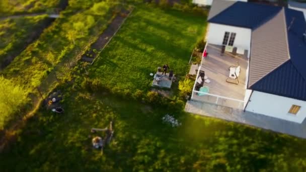 High angle drone shot of a house in small town with green yard where man is making barbecue — Stock Video