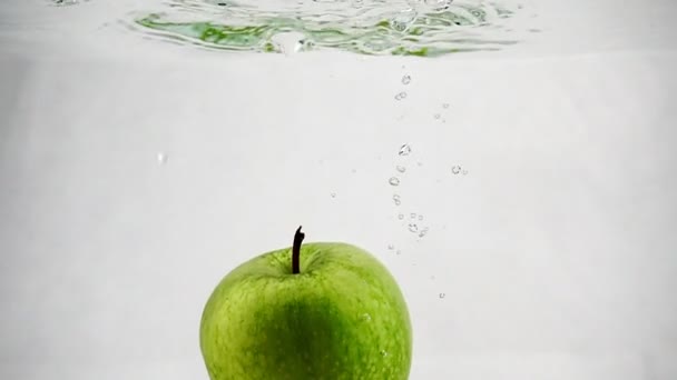 Ett grönt äpple faller i vattnet med bubblor i slow motion. Frukt på isolerad vit bakgrund. — Stockvideo