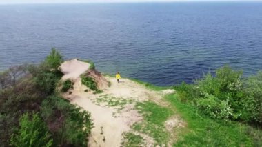 Uçurumun drone görüntüsü ve üzerinde yürüyen ve okyanusa bakan kadın.