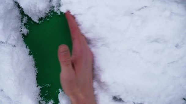 Мужская рука очищает снег, показывая зеленый фон в крупном плане — стоковое видео