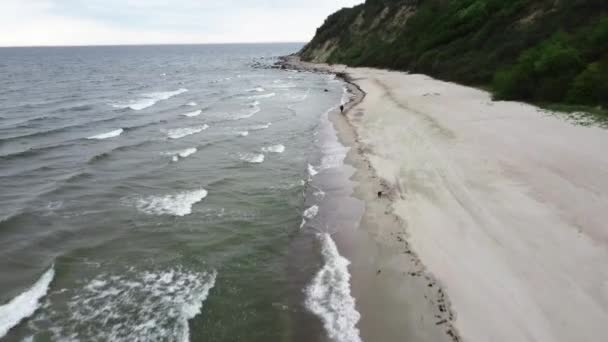 L'uomo si muove sulla costa tra l'oceano tempestoso e la scogliera verde filmata dall'alto — Video Stock