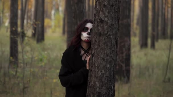 Bruxa com maquiagem de Santa Muerte está se escondendo atrás da árvore e aparece novamente — Vídeo de Stock